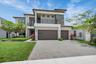 Contemporary two-story residence featuring a paver driveway, multiple garage doors, a second-story balcony with metal railing, and a stone accent faca