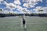 Multiple hard tennis courts featuring perimeter fencing, professional-grade nets, court lighting, and a shaded seating area