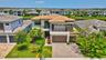 Contemporary architecture featuring a tile roof, stone facade accents, a paver driveway, an attached garage, and mature landscaping