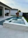 Outdoor living space featuring a rectangular pool with an integrated spa, a built-in outdoor kitchen with a grill, and a covered patio area