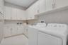 Laundry room featuring white cabinetry, light-toned countertops, a utility sink with a chrome faucet, and patterned wallpaper