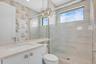 Bathroom featuring a glass-enclosed shower with a transom window and marble-look wall tiling
