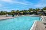 Expansive swimming pool area with paver decking, multiple sun loungers, cabanas, and mature palm trees