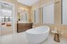 Freestanding soaking tub with a floor-mounted faucet, dual vanity with undermount sinks, and a large wall mirror with overhead lighting