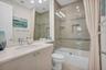 Bathroom featuring a large vanity with an integrated sink and light-colored countertop, built-in cabinetry, a toilet, and a combination tub/shower wit