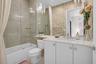 Contemporary bathroom featuring a tub with a glass panel enclosure, a single vanity with a white countertop, and a wall-mounted mirror