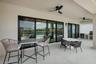 Expansive covered patio featuring light-toned tile flooring, multiple sliding glass doors, two ceiling fans, and an outdoor kitchen area with built-in