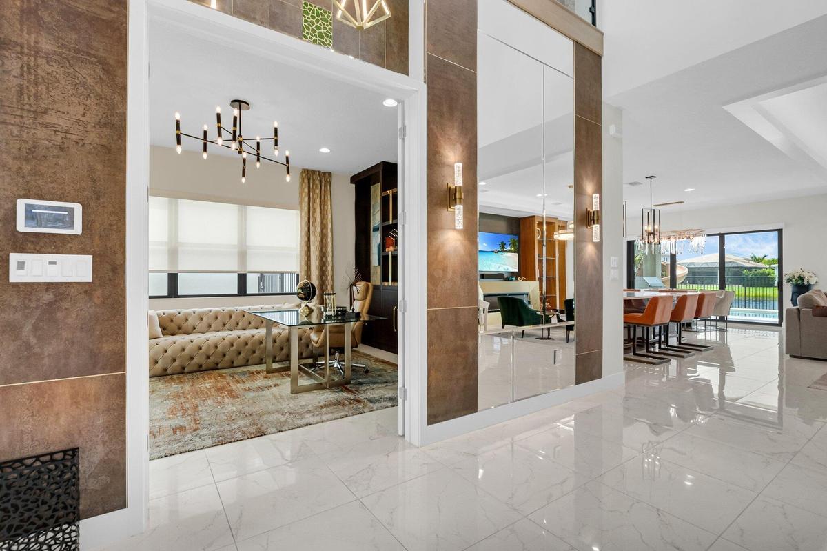 Expansive main living area featuring glossy white tile flooring, a large mirrored wall with integrated sconce lighting, and a view into an adjacent ro