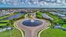 Community entrance featuring a circular water feature with multiple fountains, manicured landscaping, and contemporary signage
