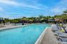 Expansive outdoor swimming pool area featuring multiple pools, paved decking, numerous lounge chairs, shaded cabanas, and mature palm trees