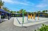 Expansive splash pad area featuring vibrant water play structures, surrounded by cabanas with blue fabric coverings, and abundant palm trees