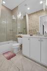 Contemporary bathroom featuring a white vanity with integrated sink, full-height wall mirror, tiled flooring, and a tub with glass shower enclosure