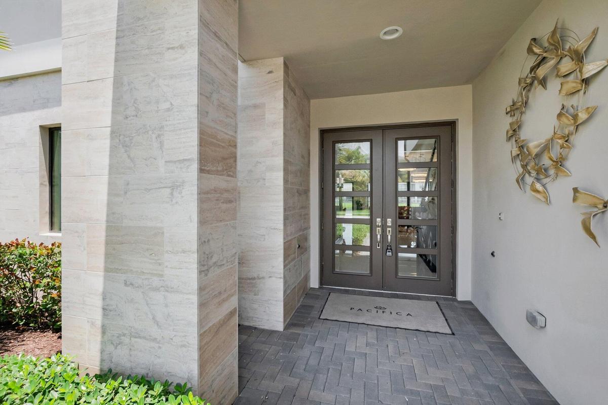 Double entry doors with divided lites, recessed lighting, herringbone pattern paver flooring, and vertical stone-clad architectural columns