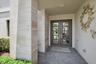 Double entry doors with divided lites, recessed lighting, herringbone pattern paver flooring, and vertical stone-clad architectural columns