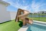 Private pool area featuring a spiral water slide, artificial turf landscaping, white perimeter wall, and a black metal fence bordering a water feature