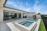 Expansive outdoor living area featuring a rectangular pool and integrated spa, a covered patio with a ceiling fan, and a built-in outdoor grill statio