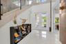 Double entry doors with multiple glass panels, a contemporary console table, polished tile flooring, a staircase with glass railings, and a wall-mount