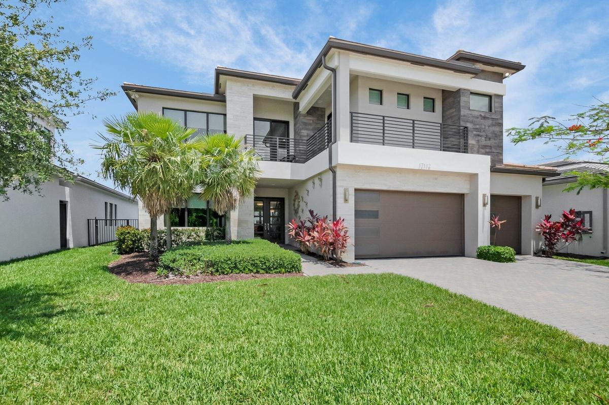Contemporary exterior featuring a stone and stucco facade, an integrated two-car garage, a second-story balcony with horizontal railings, mature lands