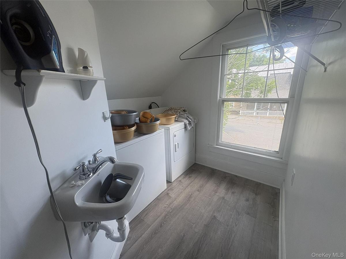 Wall-mounted utility sink, white shelving, wood-finish flooring, and a single window
