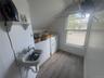 Wall-mounted utility sink, white shelving, wood-finish flooring, and a single window