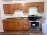 Wood-finish cabinetry with dark hardware, stainless steel range with gas cooktop, double basin sink with chrome faucet, laminate countertops, and wood