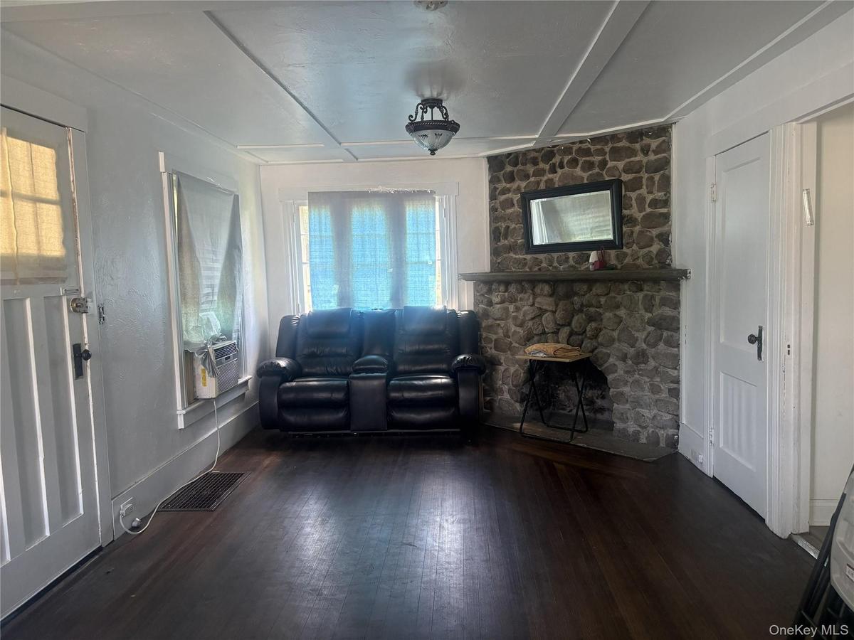 Stone-clad fireplace with a substantial mantel, dark wood-finish flooring, white paneled doors, and a decorative ceiling fixture
