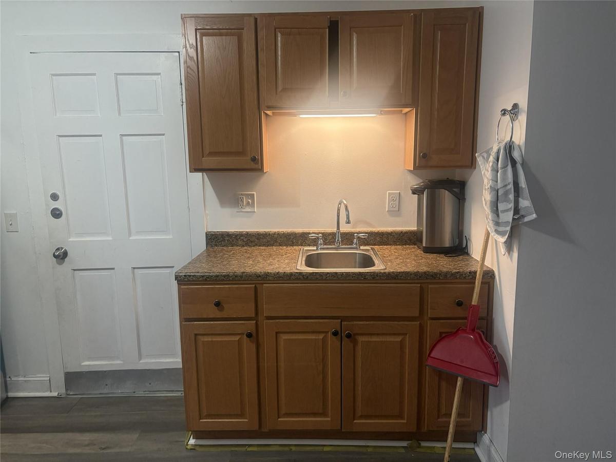 Kitchenette featuring wood cabinetry, laminate countertops, stainless steel sink, and wood-finish flooring