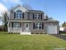 Traditional-style house featuring an attached garage, covered porch, driveway, and a front lawn