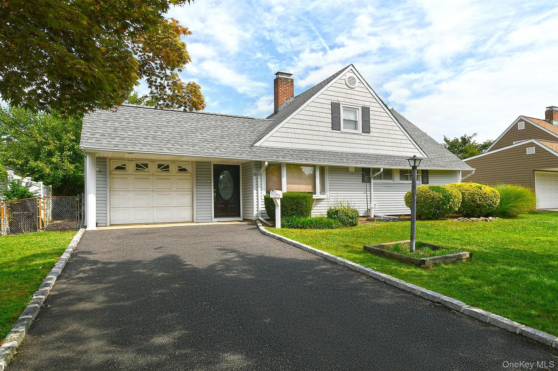 Light-colored siding exterior with a dark entry door, attached garage with panel door, asphalt driveway, and a well-maintained lawn