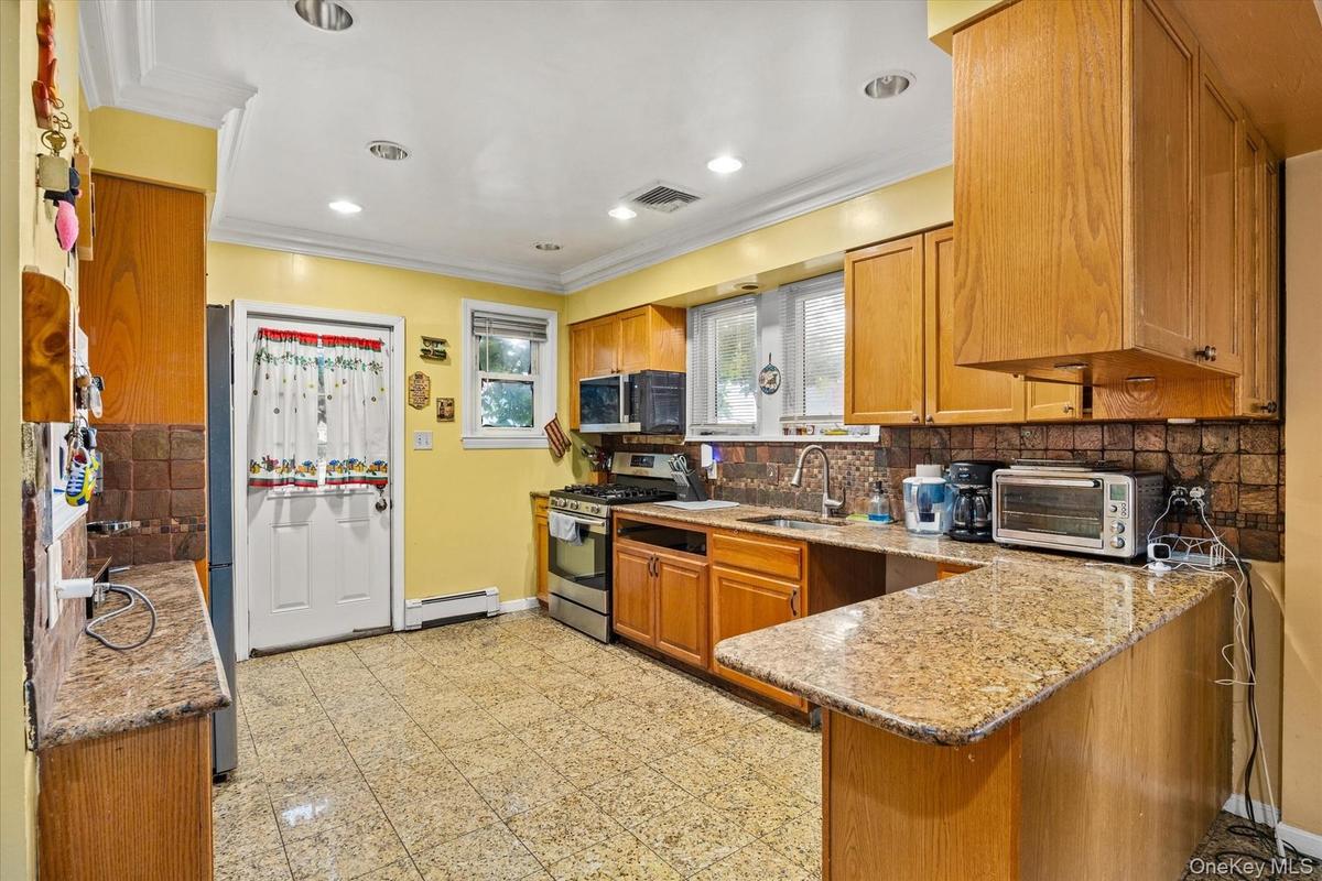 Kitchen featuring wood cabinetry, granite-finish countertops, tile backsplash, stainless steel appliances, and recessed lighting