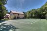 Full-size tennis court with a perimeter fence, adjacent to a residence with shingle siding and dark-trimmed windows