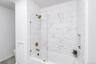 Bathtub with glass shower partition, gold-finish fixtures, and marble-look subway tile surround