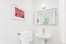 Pedestal sink with chrome faucet, wall-mounted mirror with rounded corners, and a chrome towel bar