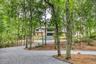 Wooded property with a gravel driveway, mature trees, and a multi-level home featuring gables and wood siding
