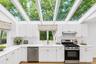 White cabinetry with brass hardware, stainless steel appliances, light wood-finish flooring, and a vaulted ceiling with exposed beams and skylights