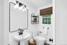 White pedestal sink with matte black faucet, framed mirror, and modern vanity lighting