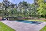 Swimming pool with integrated spa, expansive paver patio, built-in outdoor kitchen, tiered landscaping, and mature perimeter trees