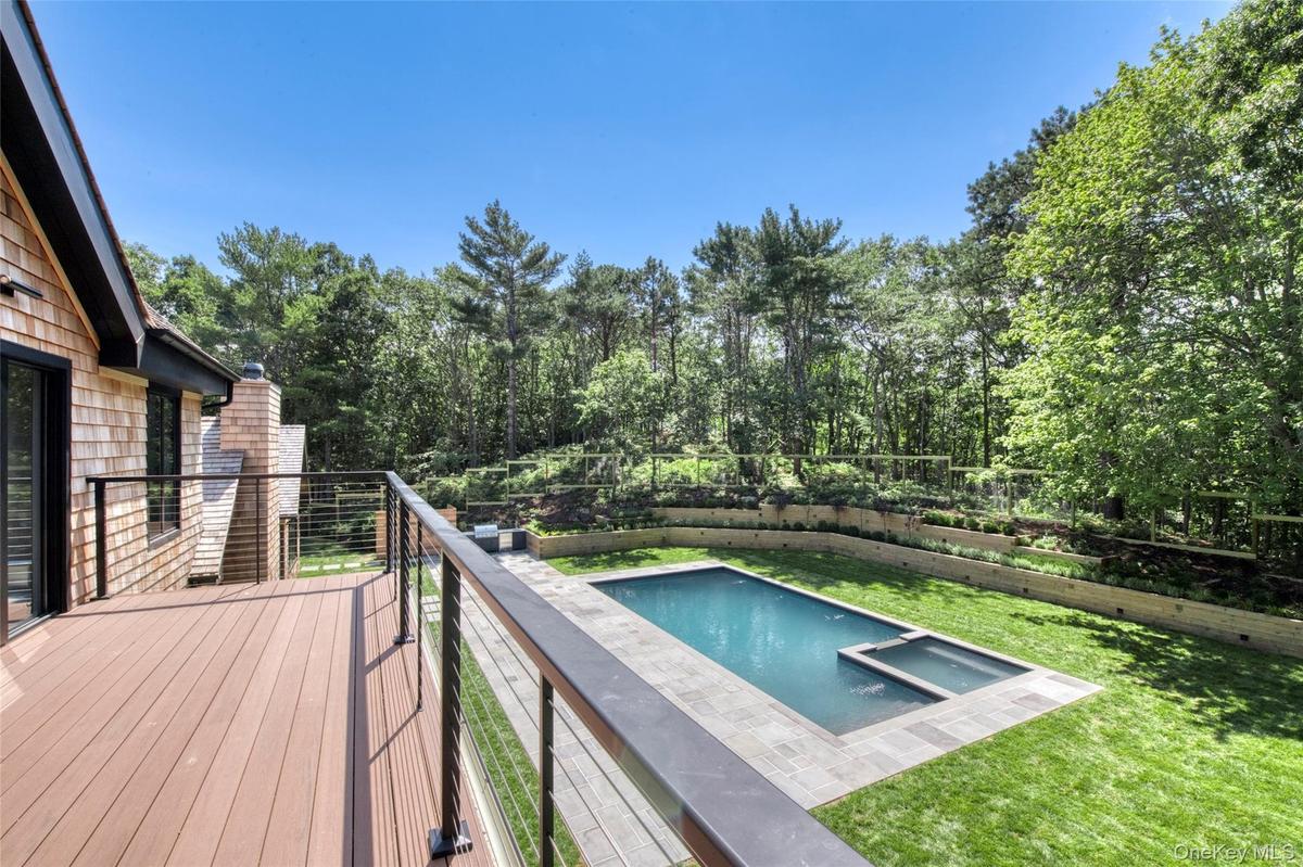 Expansive deck with cable railing, shingle siding, rectangular swimming pool, integrated spa, and tiered landscaping
