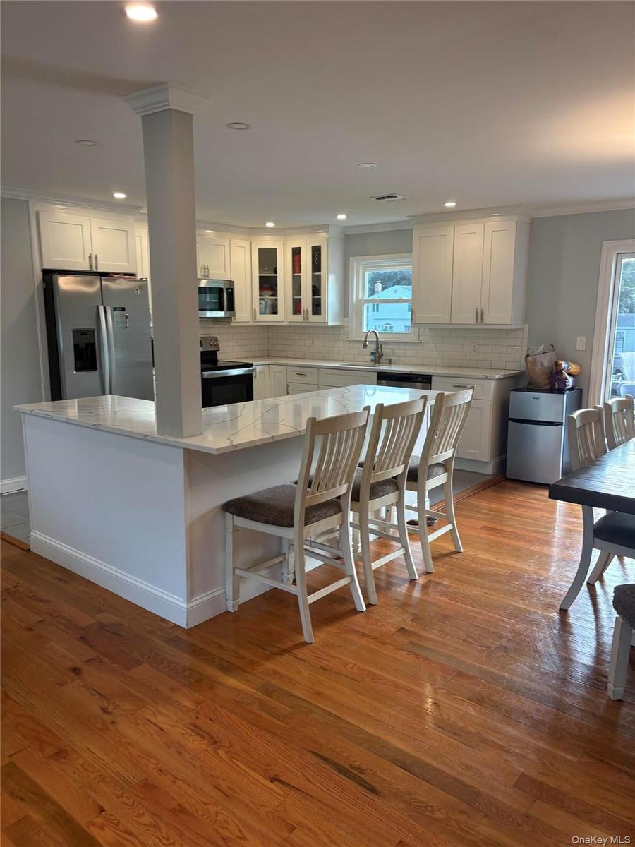 Kitchen featuring white shaker cabinetry, stainless steel appliances, light-toned countertops, and wood-finish flooring