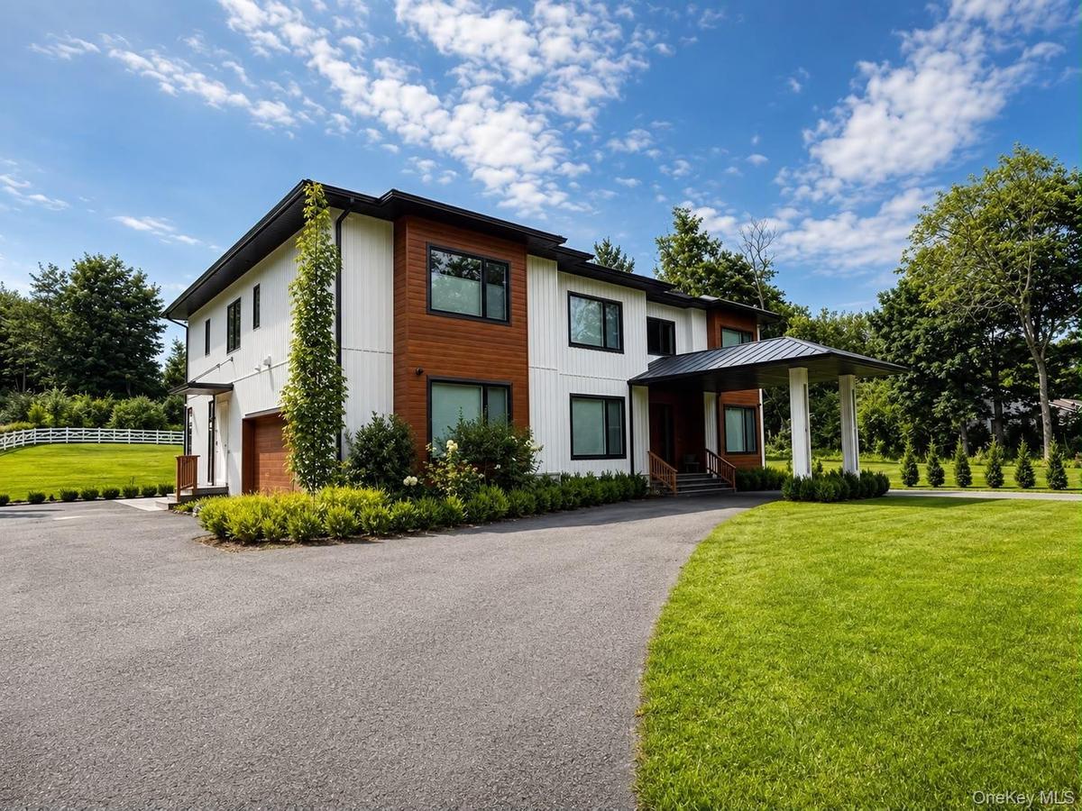 Contemporary exterior featuring white siding and wood-finish accents, a covered entry, a paved driveway, and manicured landscaping