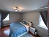 Second bedroom with california-king-size bed and hardwood flooring, light gray wall paint, and a modern ceiling light fixture, two windows allow cross