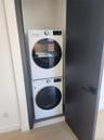 Stackable washer and dryer appliances within a dedicated closet, featuring a dark wood-finish door and contemporary hardware