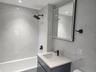 Full-height tiled walls, recessed lighting, matte black fixtures, integrated bathtub, and a floating vanity with a vessel sink