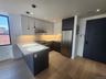 Modern kitchen featuring light wood-finish flooring, stainless steel appliances, dark lower cabinetry, light upper cabinetry, and a white countertop w