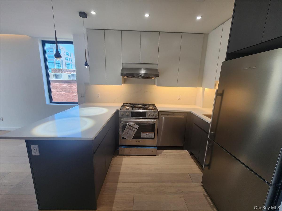 U-shaped kitchen featuring wood-finish flooring, stainless steel appliances, white countertops, dark lower cabinetry, and light upper cabinetry