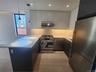 U-shaped kitchen featuring wood-finish flooring, stainless steel appliances, white countertops, dark lower cabinetry, and light upper cabinetry