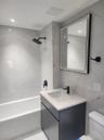 Bathroom featuring a white subway tile bathtub surround, modern black shower fixtures, a dark wood-finish vanity with an integrated sink, a light-colo