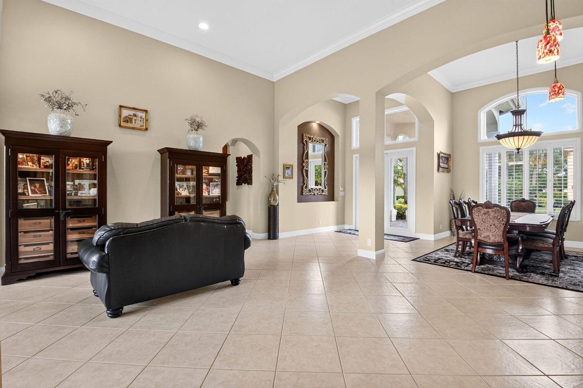Arched doorways with crown molding, high ceilings, large windows with plantation shutters, and light-colored tile flooring