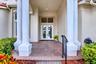 Portico entry featuring large columns, double glass-paneled doors, brick paver flooring, and a wrought iron handrail