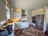 White cabinetry with integrated lighting, stainless steel appliances, herringbone flooring, and cooktop with a stainless steel range hood